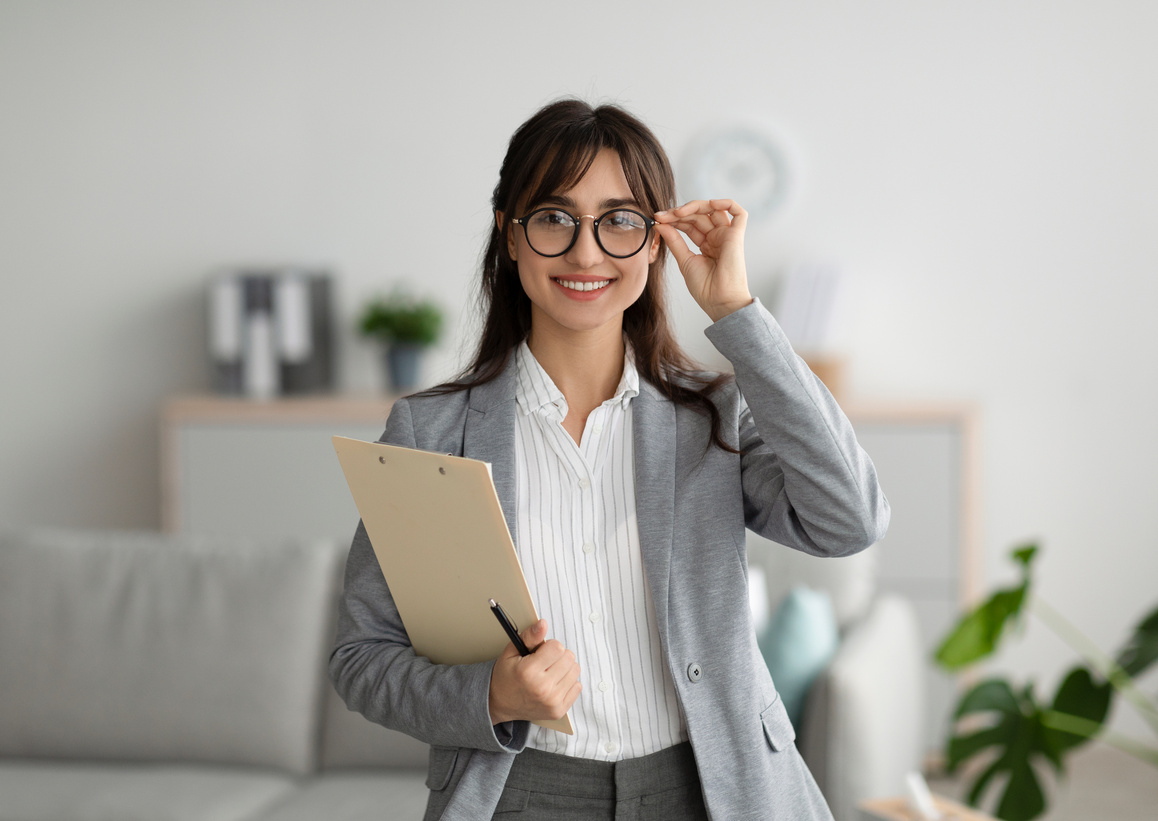 Successful Psychologist. Portrait of Arab Female Psychologist Holding Clipboard, Smiling at Camera in Modern Office